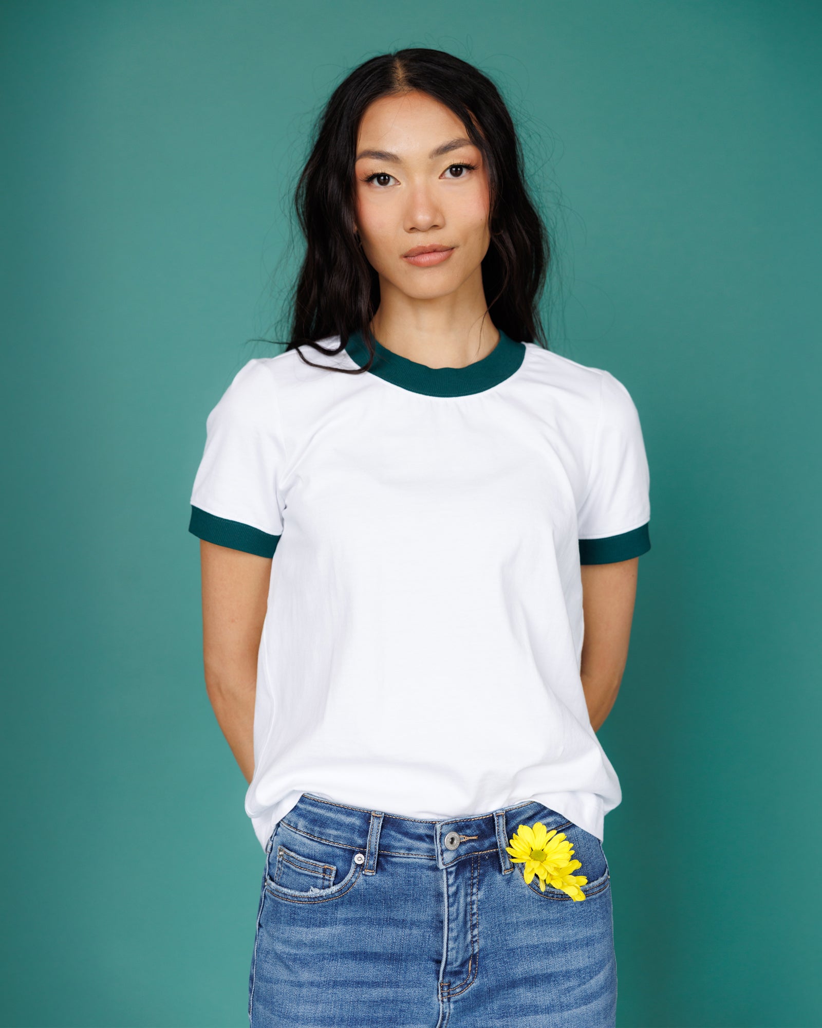 Person wearing a white ringer shirt with green trim against a teal background