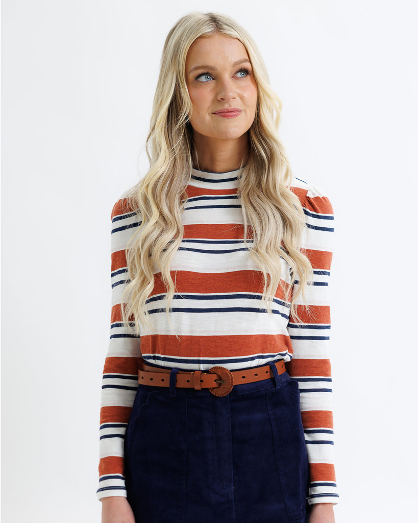 Woman wearing a striped sweater with orange, white, and navy colors on a plain background