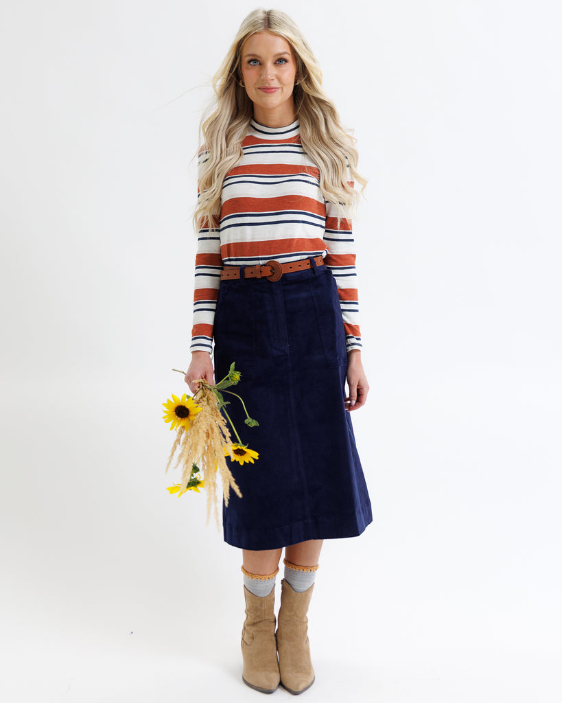Woman wearing a striped sweater and navy skirt holding sunflowers on a white background