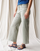 Person wearing light gray pants and blue sandals on a neutral background