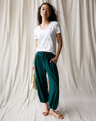 Woman wearing a white t-shirt with small prints and teal pants against a plain background