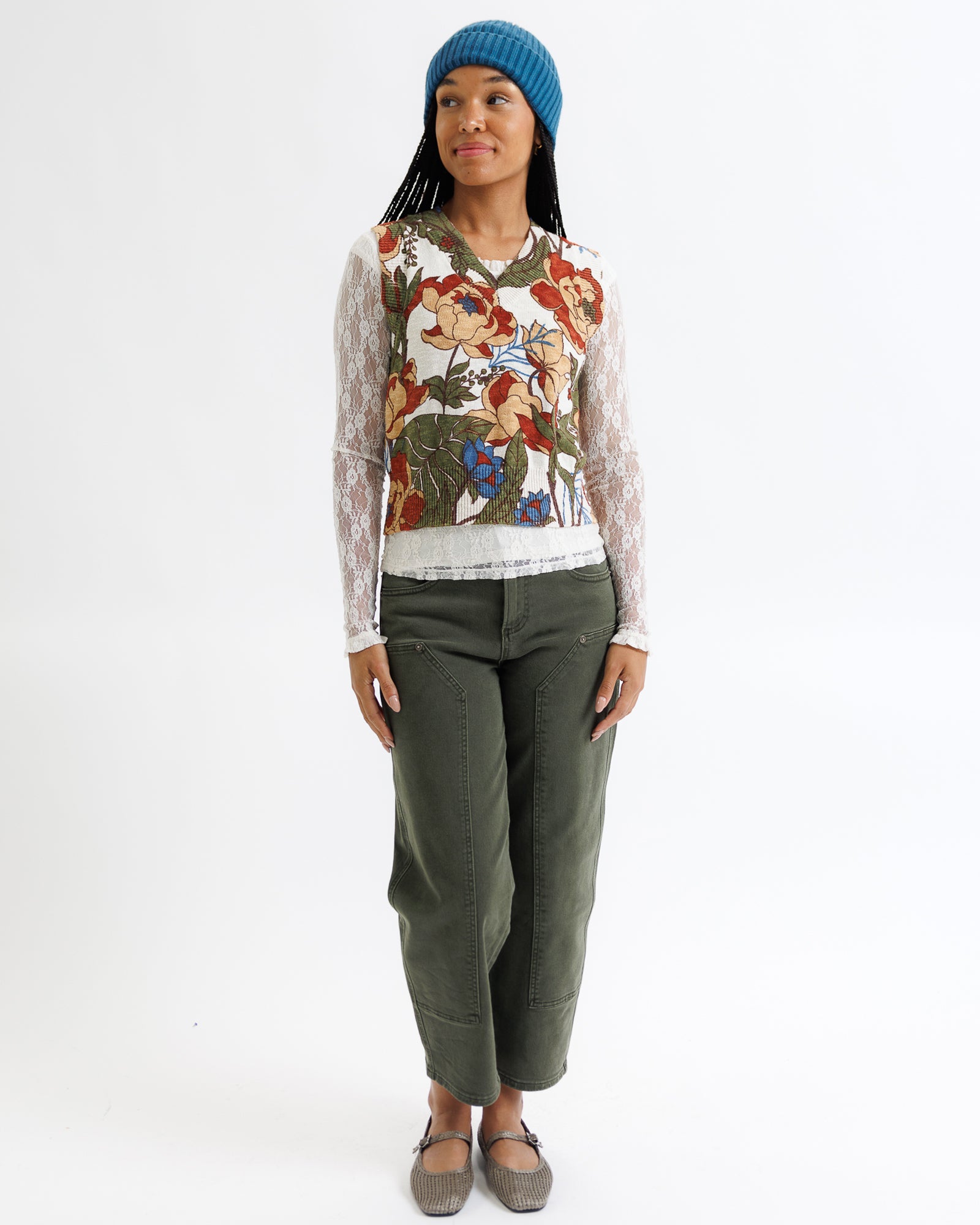 Person wearing a floral sweater and green pants on a white background