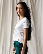 Woman wearing a white blouse with floral embellishments against a neutral background