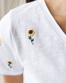 White shirt with embroidered sunflowers on a plain background