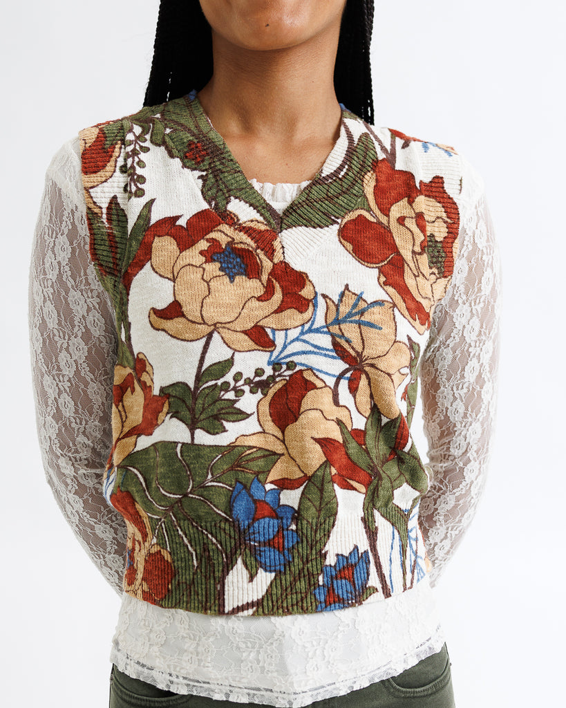 Woman wearing a floral embroidered top with a white lace overlay on a plain background