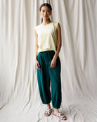 Woman wearing a light-colored top and teal pants against a plain background