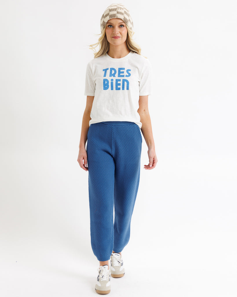 Woman wearing a white t-shirt with 'TRES BIE' text and blue pants on a white background