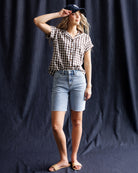 Woman wearing a checkered shirt, denim shorts, and a cap against a dark background