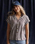 Image of a woman wearing a brown gingham top against a dark blue background