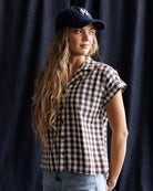 Woman wearing a checkered shirt and cap against a dark curtain