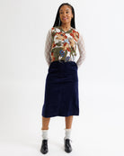Person wearing a floral sweater, navy skirt, and white socks on a white background