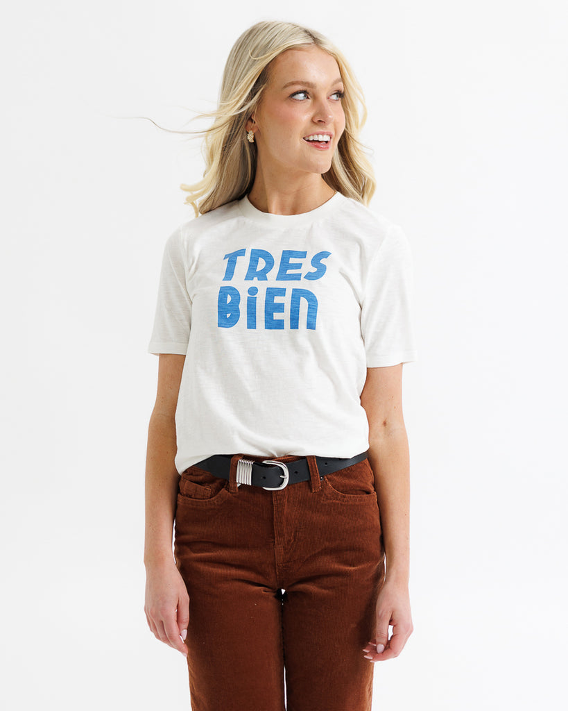 Woman wearing a white t-shirt with 'TRES BIEN' text on a plain background