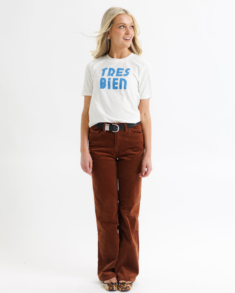 Woman wearing a white t-shirt with 'TRES BIEN' text and brown pants on a white background