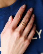 A close-up of a person's hand wearing two thin gold rings, resting on their blue sweatshirt.