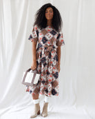 Front view of a patchwork floral midi dress featuring short sleeves, a crew neckline, and a gathered A-line skirt cinched with a matching tie belt at the waist.