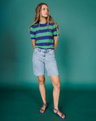 Woman wearing a striped shirt and denim shorts against a teal background