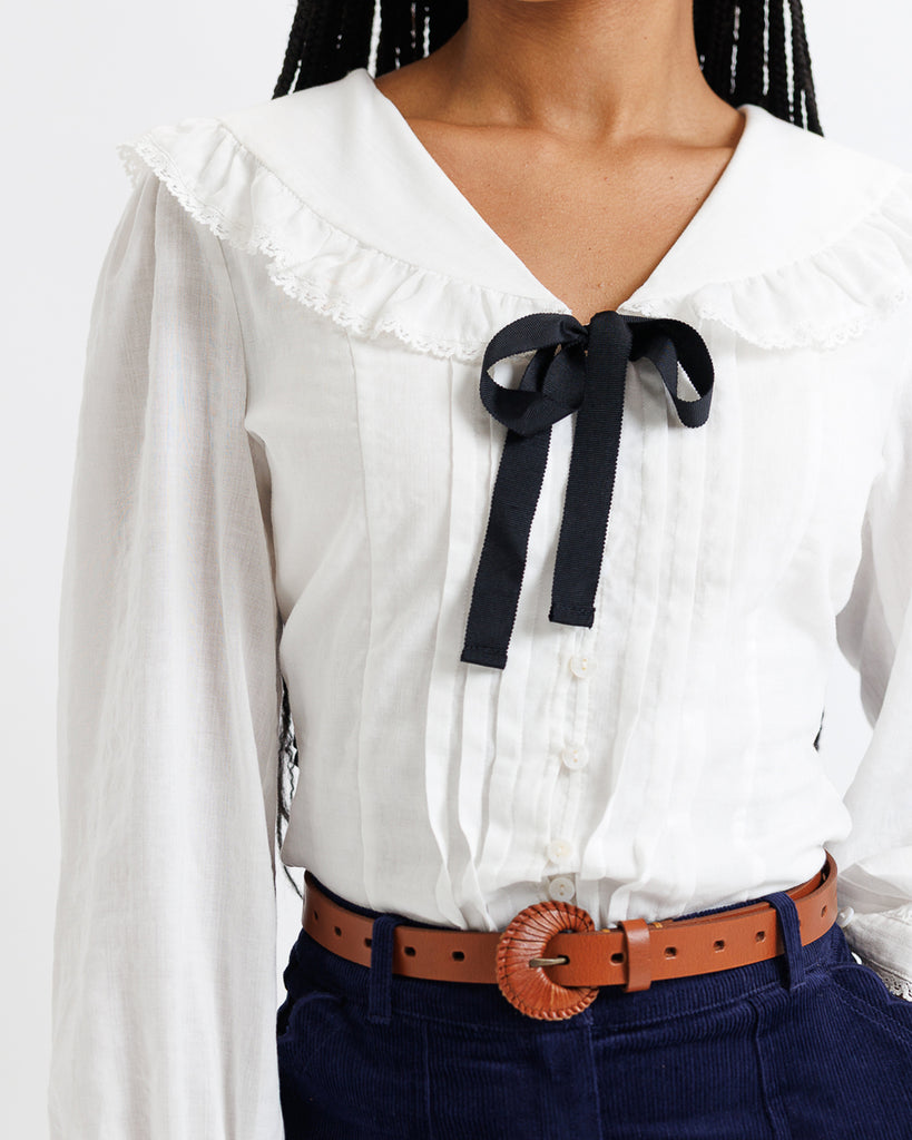 White blouse with a black bow and blue pants on a white background