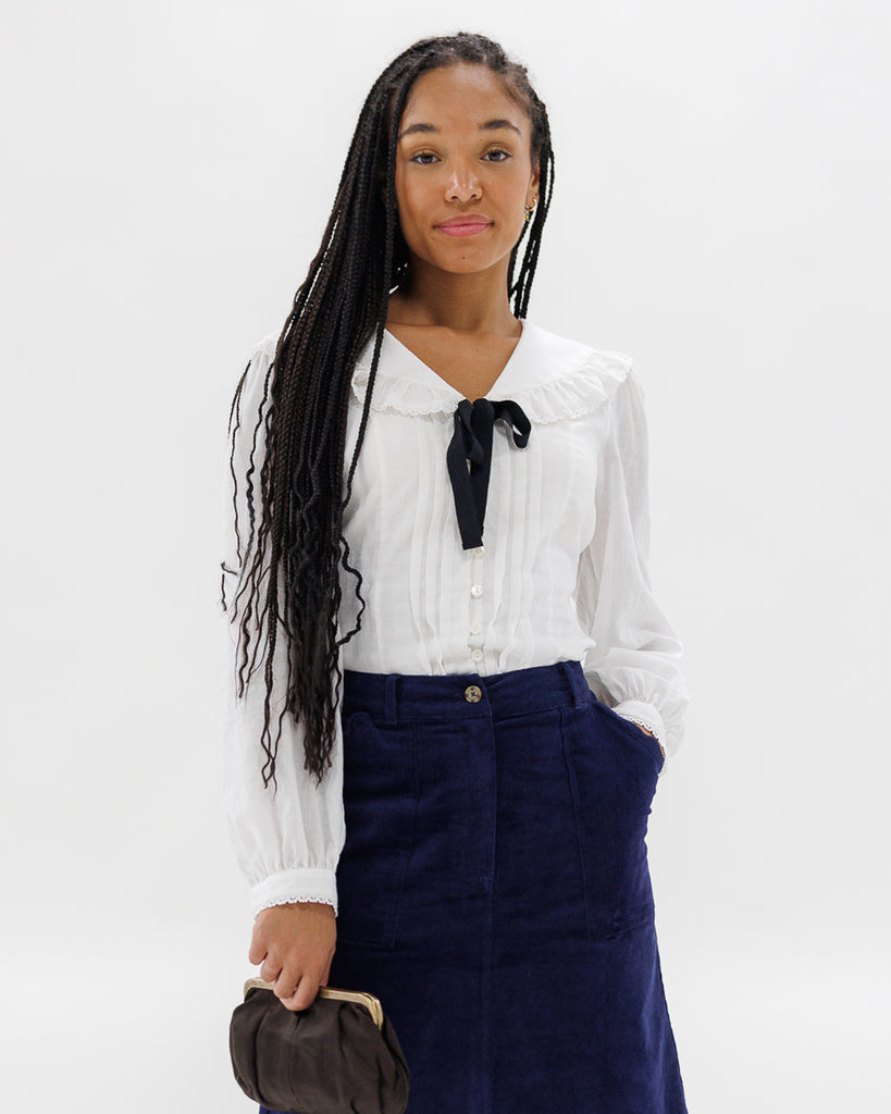 Woman wearing a white blouse with a black tie and a navy skirt on a white background