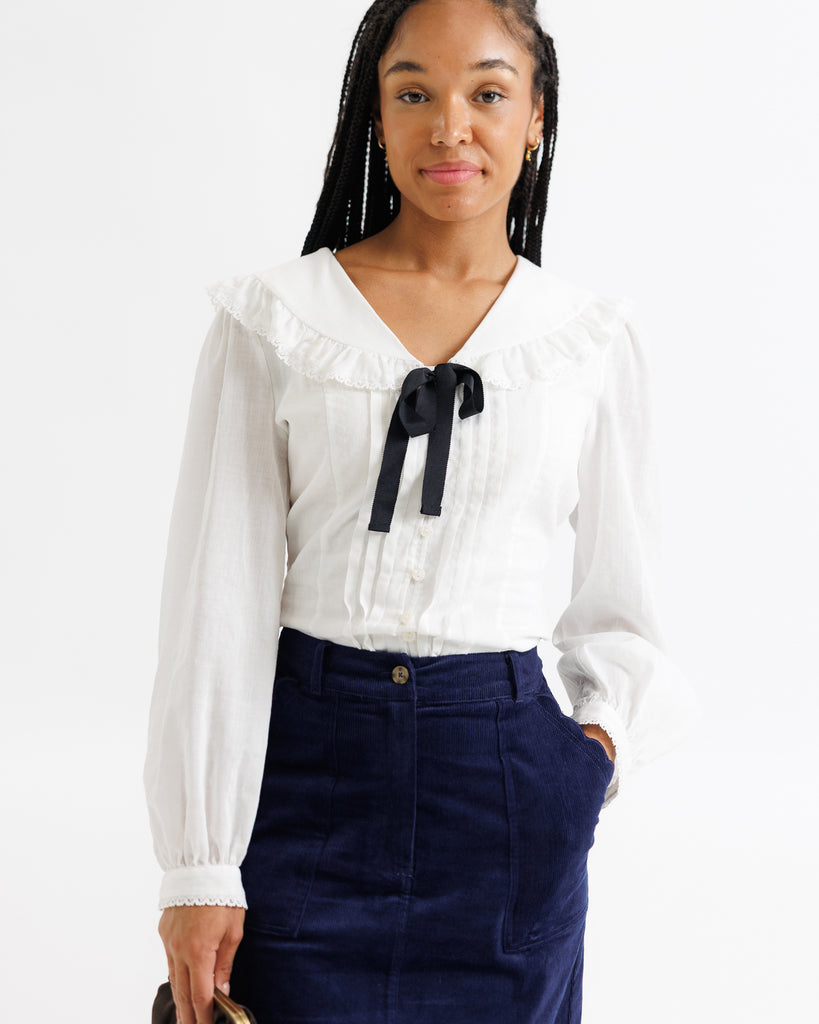 Woman wearing a white blouse with a black ribbon and navy pants on a white background
