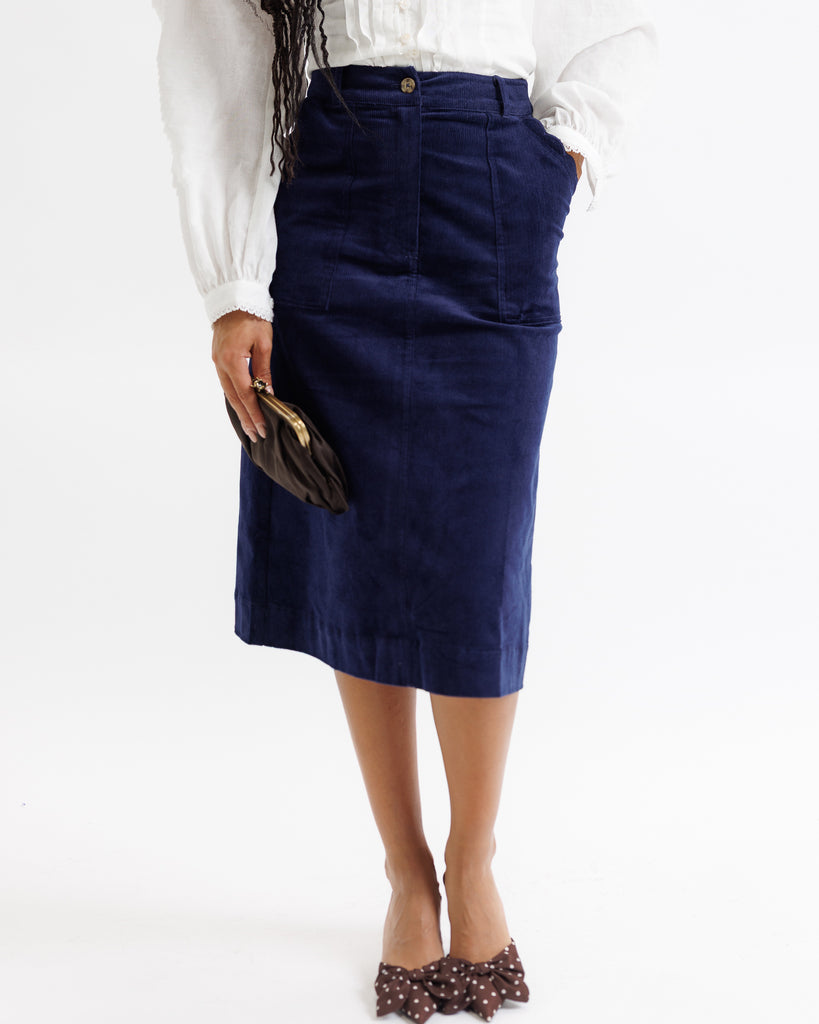 Person wearing a navy blue skirt with a white blouse on a white background