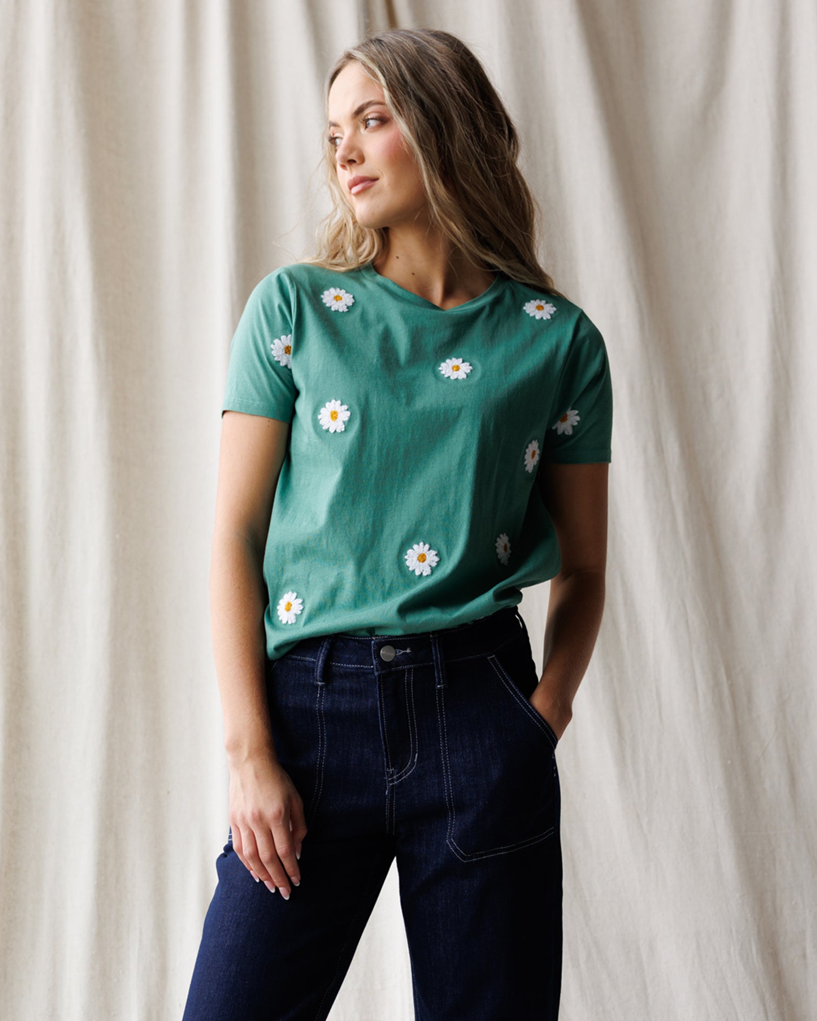 Woman wearing a green t-shirt with white floral patterns against a beige curtain background
