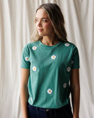 Woman wearing a green t-shirt with white daisy flowers on a plain background