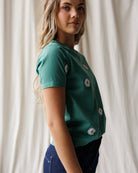 Woman wearing a green t-shirt with white daisy patterns against a plain background