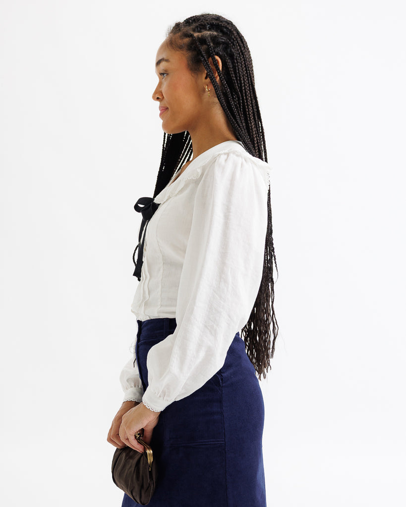 Woman wearing a white blouse and dark blue pants on a white background