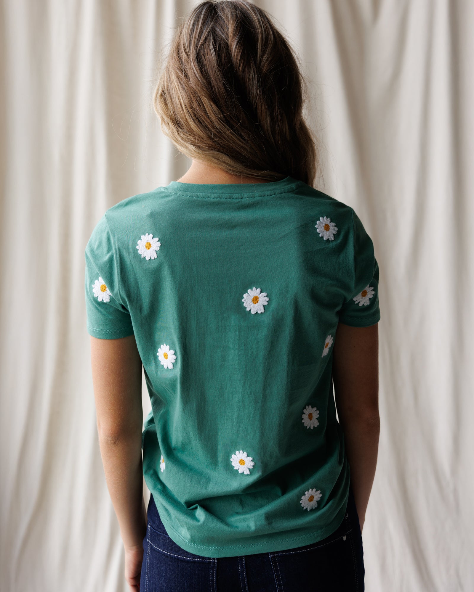 Person wearing a green t-shirt with white daisy patterns against a plain background