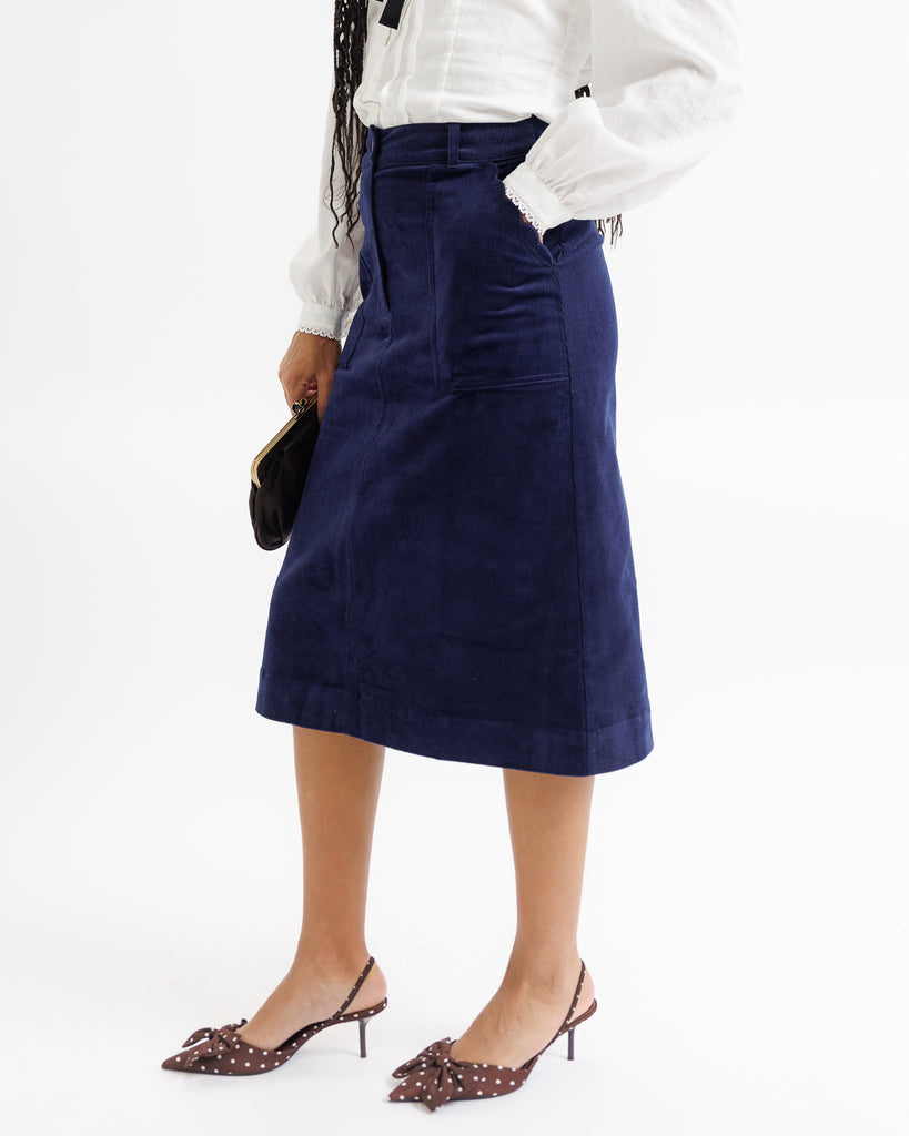 Person wearing a navy blue skirt with a white top on a white background