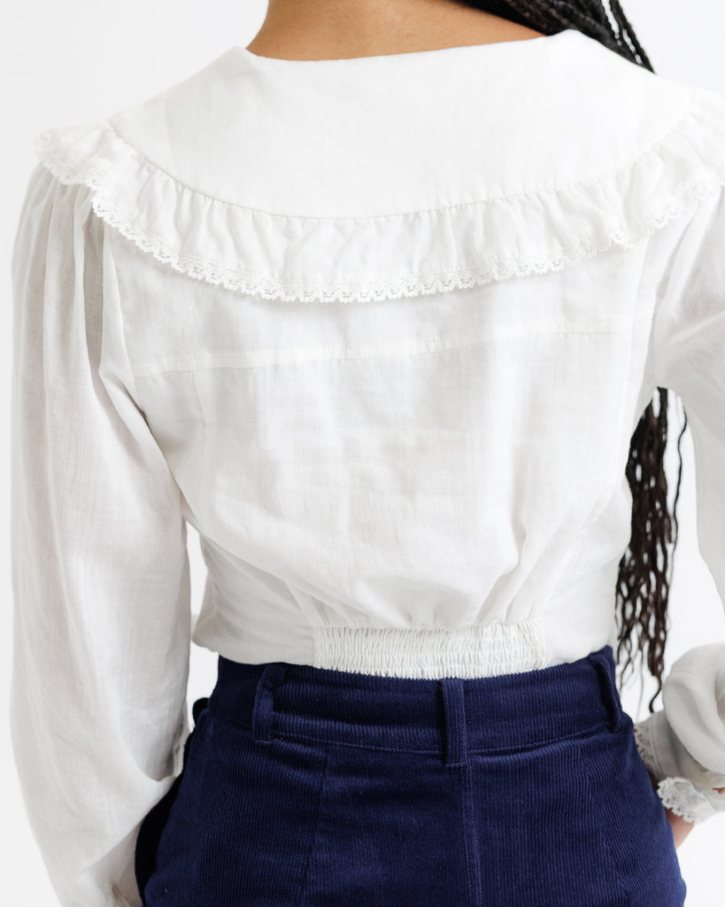 White blouse with ruffled collar and long sleeves worn by a person, with a blurred background.