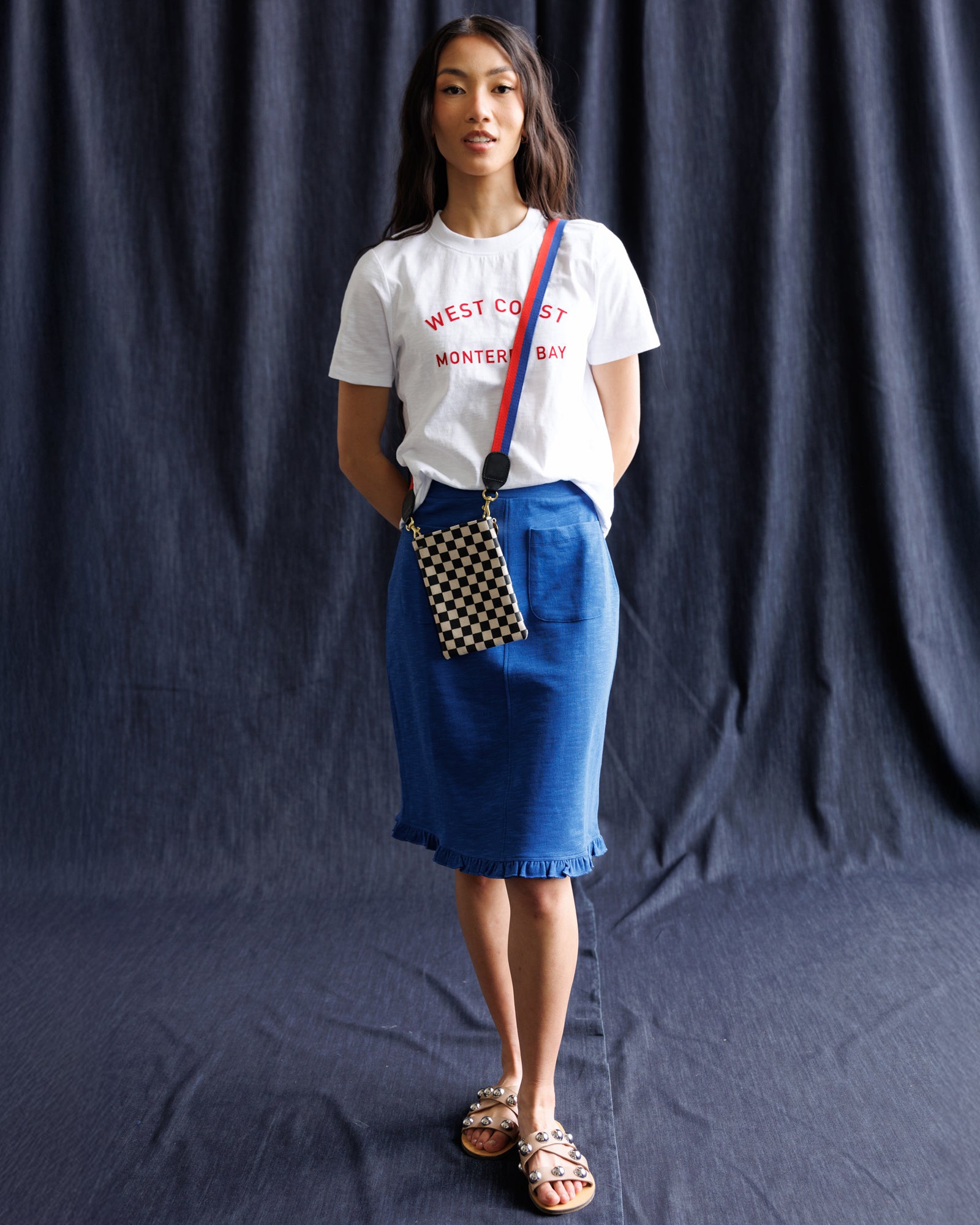 Woman wearing a white t-shirt with text and a blue skirt, standing against a dark backdrop
