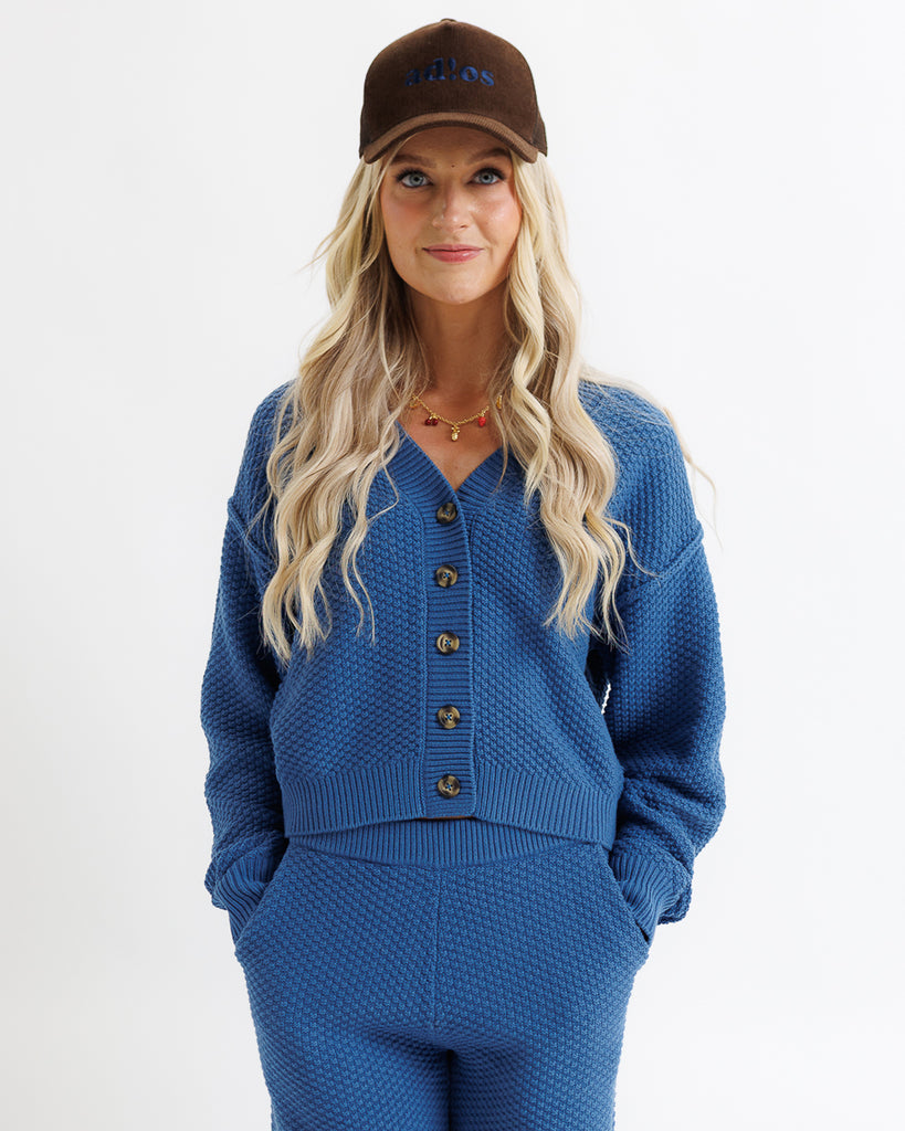 Woman wearing a blue cardigan and pants with a brown cap on a white background