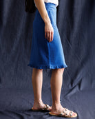 Person wearing a blue skirt with ruffled hem on a dark background