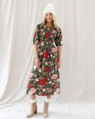 Front view of an olive green midi dress with red and cream rose print, featuring an elastic smocked bodice, split keyhole neckline, elbow-length puff sleeves, and a flowy A-line skirt