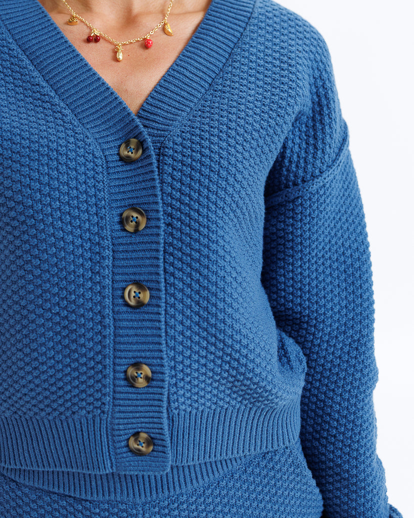 Close-up of a blue textured cardigan with buttons on a white background