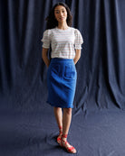 Woman wearing a striped shirt and blue skirt against a dark blue curtain.