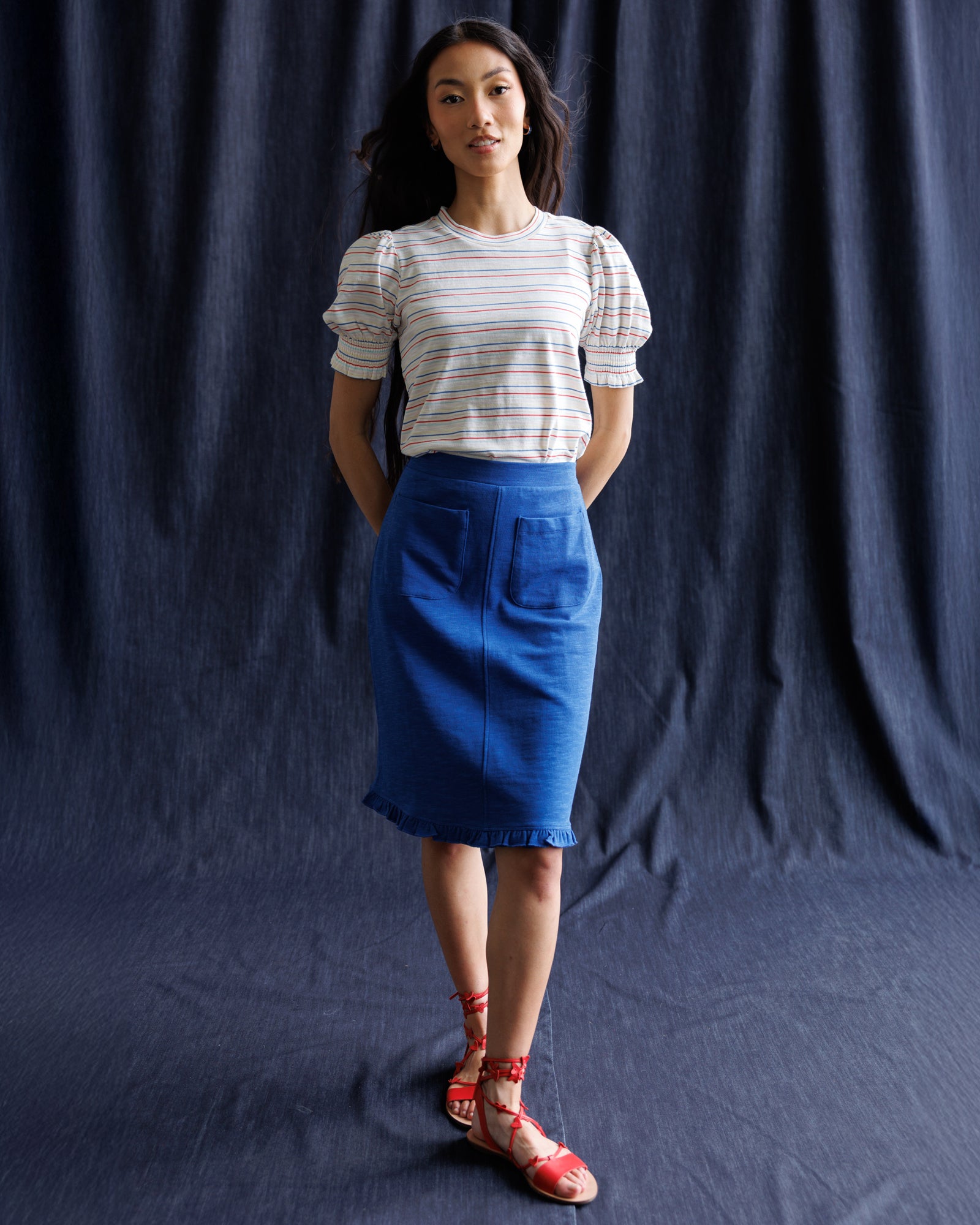 Woman wearing a striped shirt and blue skirt against a navy background