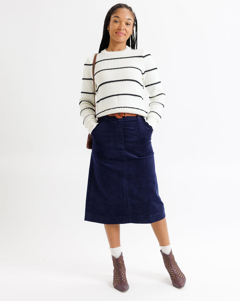 Person wearing a striped sweater and navy skirt on a white background