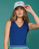 Woman wearing a blue sleeveless top and striped skirt against a teal background