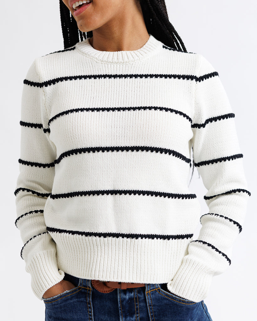 Person wearing a white sweater with black stripes on a plain background