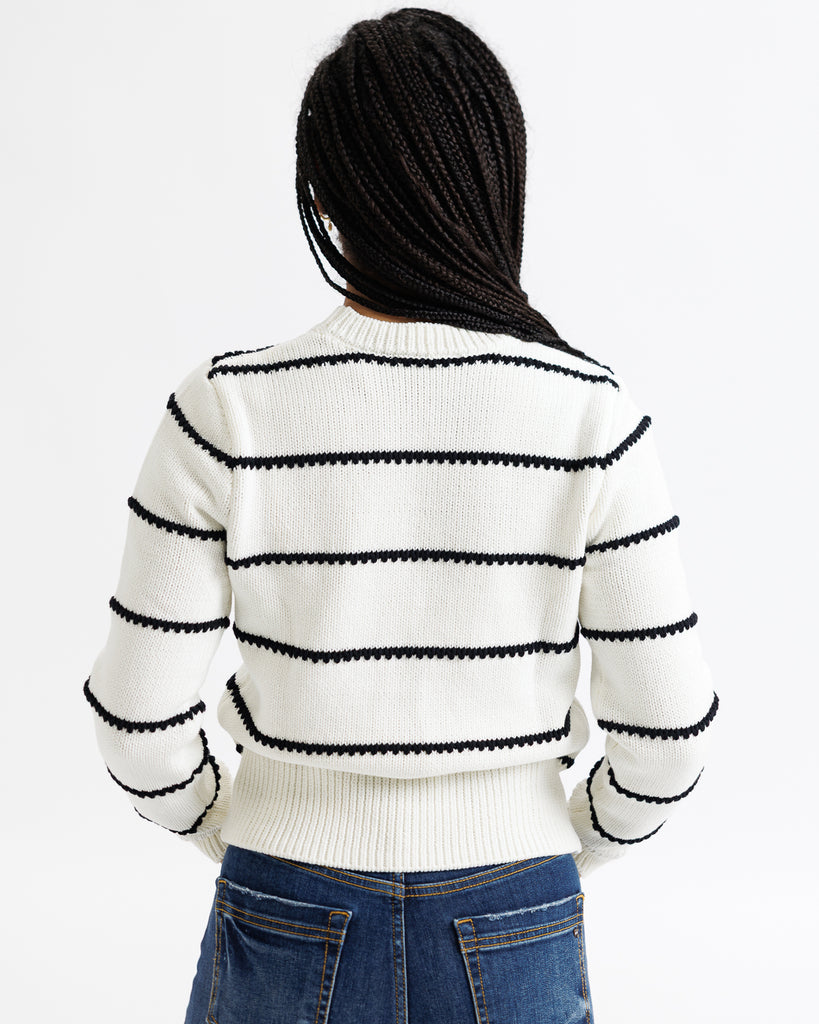Person wearing a white sweater with black stripes and blue jeans on a white background