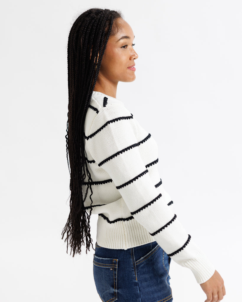 Woman wearing a white sweater with black striped patterns on a plain background