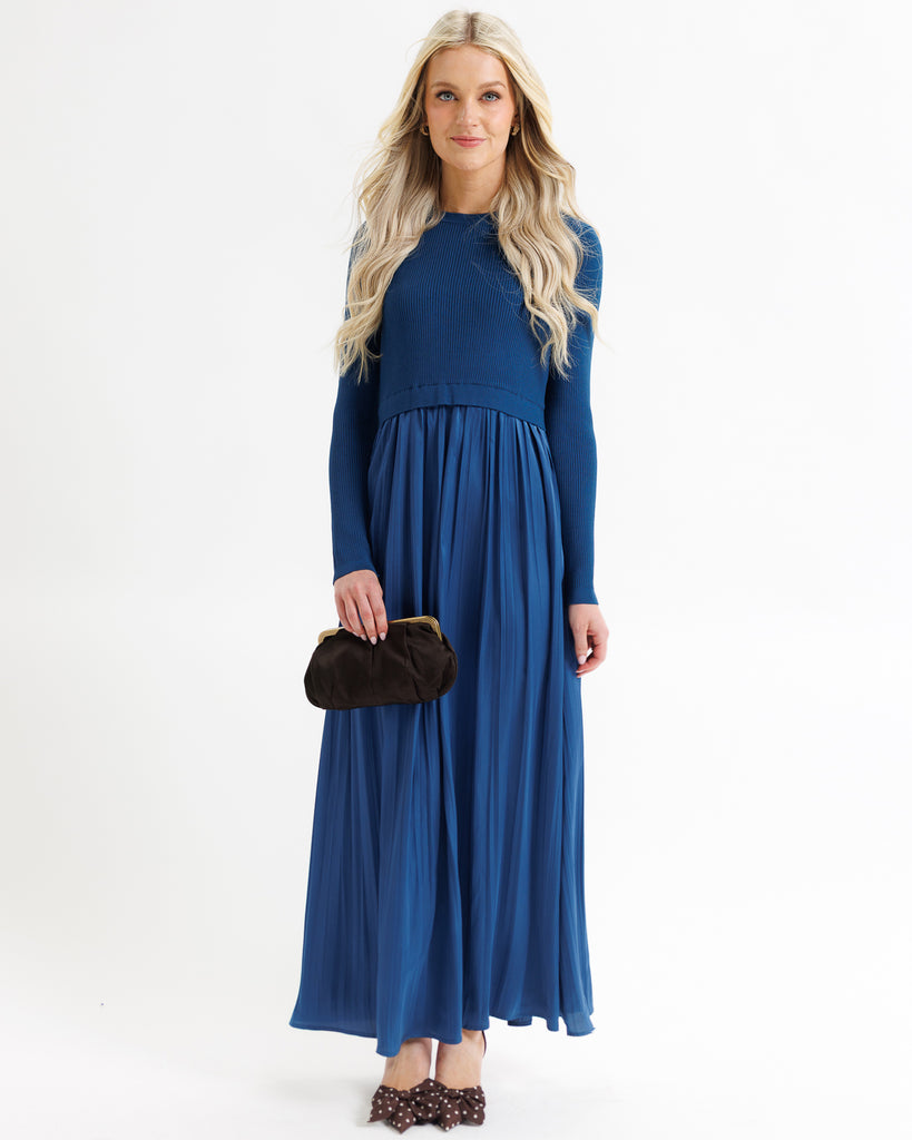 Woman wearing a blue dress holding a black clutch against a white background