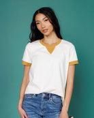 Woman wearing a white t-shirt with yellow accents and blue jeans against a teal background