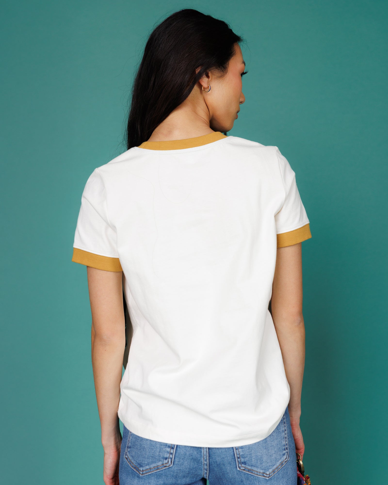 Person wearing a white t-shirt with yellow trim against a teal background