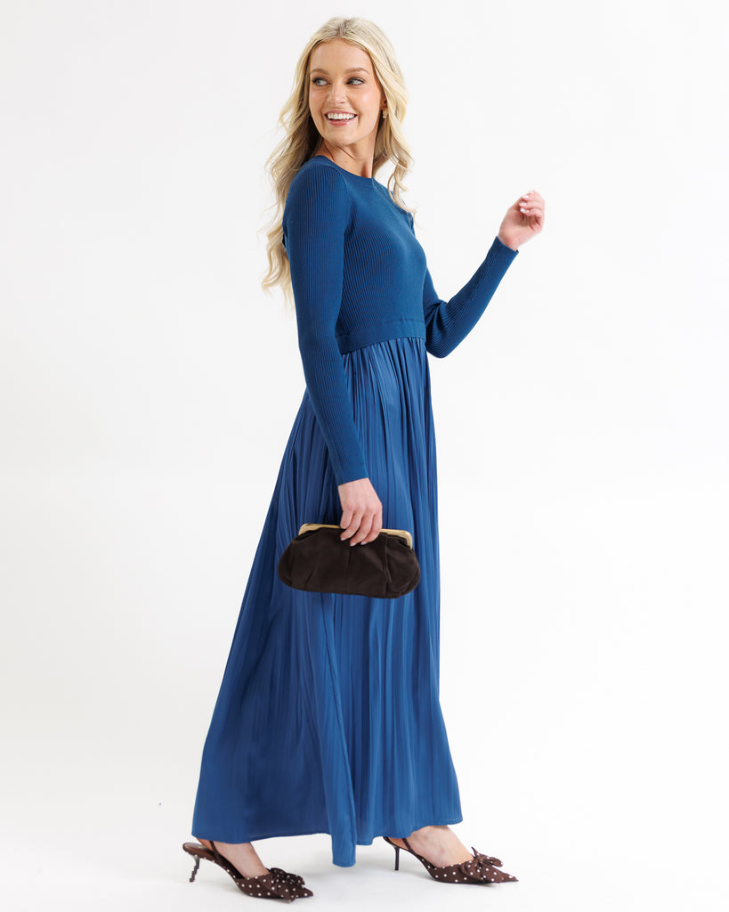 Woman wearing a blue dress holding a black clutch against a white background