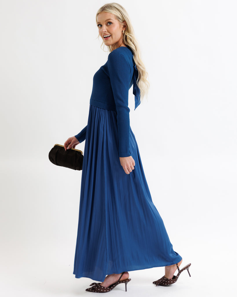 Woman wearing a blue dress holding a black clutch against a white background