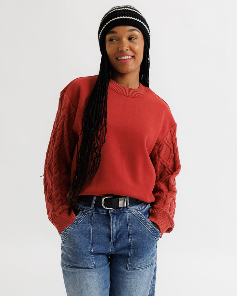 Person wearing a red sweater, blue jeans, and a black and white beanie on a plain background