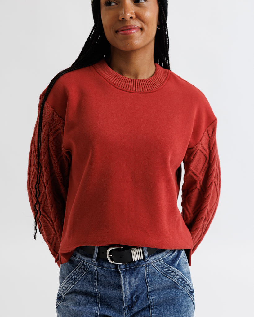 Person wearing a red sweater with ruched sleeves on a white background